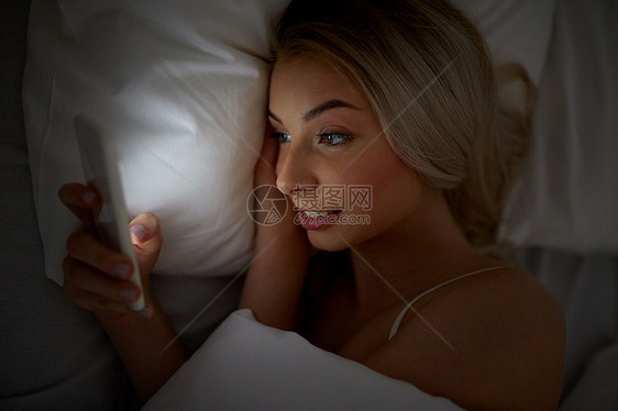 技术,互联网,沟通人的快乐的微笑轻妇女智能手机上发短信家里的卧室晚上图片