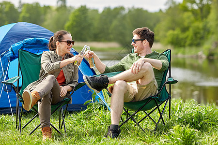 野营,旅游,徒步旅行人们的快乐的夫妇营地帐篷里碰啤酒瓶图片