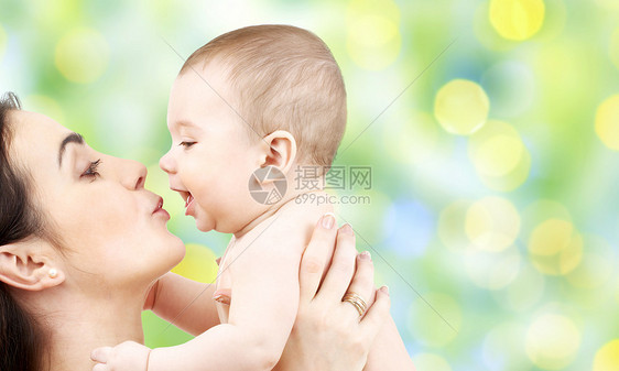 家庭,母亲,养育,人儿童保育的快乐的母亲亲吻可爱的婴儿绿色假日灯光背景图片