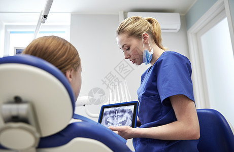 人,医学,口腔医学,技术保健女牙医平板电脑上向牙科诊所办公室的病人女孩展示牙齿X光图片