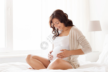怀孕,休息,人期望的快乐的孕妇坐床上,触摸她的肚子家里背景图片