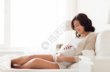 怀孕,休息,人期望的快乐的孕妇躺床上,触摸她的肚子家里背景图片