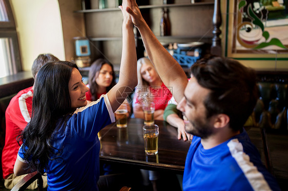 体育娱乐活动快乐的球迷朋友喝啤酒,击掌庆祝胜利酒吧酒吧,支持两支同衬衫颜色的球队图片