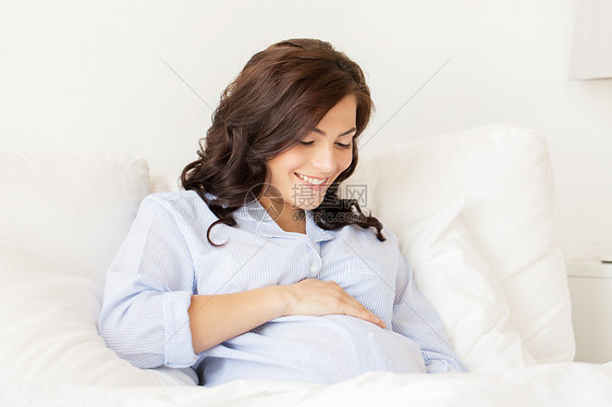 怀孕,休息,人期望的快乐的孕妇躺床上,触摸她的肚子家里图片