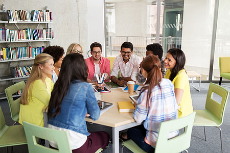 教育高中学人技术群国际学生坐桌子上,着平板电脑电脑书籍,大学里聊天图片