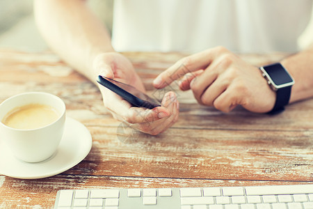 商业,技术人的近距离的男手着智能手机,戴着手表与咖啡键盘木桌上图片