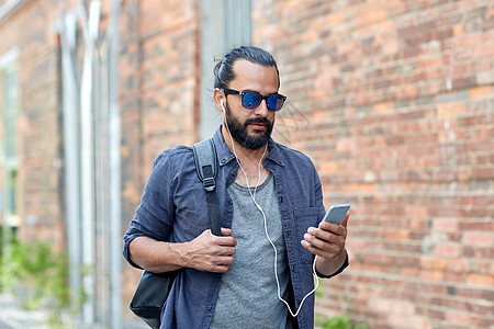 人,技术,旅游旅游带耳机,智能手机袋子的人沿着城市街道走,听音乐图片