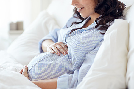 怀孕,休息,人期望的快乐微笑的孕妇躺床上,触摸她的肚子家里背景图片