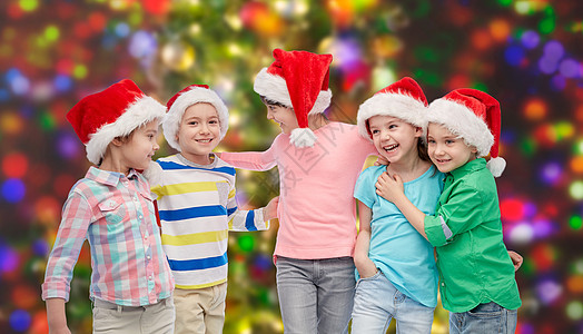 童,诞节,假日,友谊人的群快乐的微笑的孩子戴着诞老人的帽子拥抱节日的灯光背景上图片