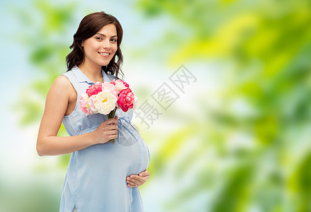 怀孕,母亲,假期,人期望的快乐的孕妇,鲜花抚摸她的大肚子绿色的自然背景图片