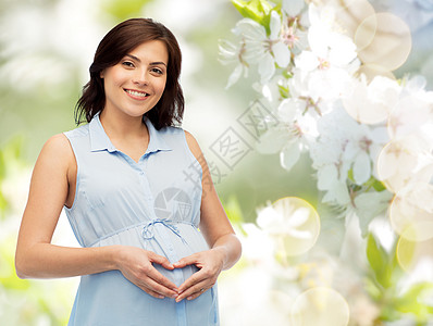 怀孕,爱,人期望的快乐的孕妇自然的春天樱花背景下腹部心脏手势图片