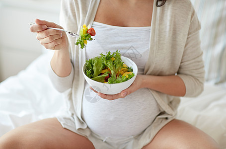 怀孕,健康的食物人们的接近快乐的孕妇家里的床上吃蔬菜沙拉图片