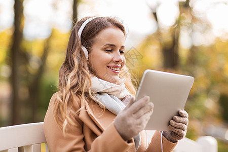 季节,技术人的美丽的快乐轻女子与平板电脑耳机听音乐,坐长凳上的秋天公园图片