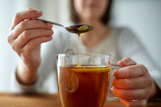 健康食品,饮食民族科学的密切妇女添加蜂蜜与柠檬茶杯图片