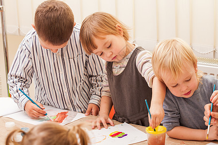 三个孩子幼儿园里学会用画笔水彩画纸上画画孩子们正画画图片