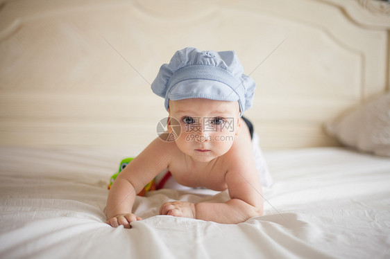 微笑的婴儿戴着蓝色的帽子,床上玩着辆玩具车,看着相机床上的婴儿图片