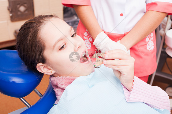 个女孩试图为牙齿牙套建立个固定器,坐牙科椅子上图片