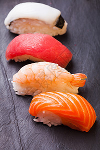 特写四套寿司与鲑鱼,金鱼,扇贝虾黑色背景图片