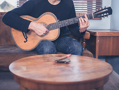 个轻人坐家里的沙发上,客厅里弹吉他,张咖啡桌,前台个烟灰缸支雪茄背景图片