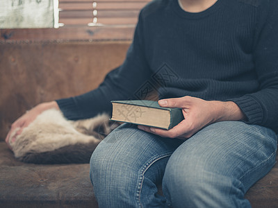 个轻人只睡猫坐沙发上,手里着本绿色的大书图片