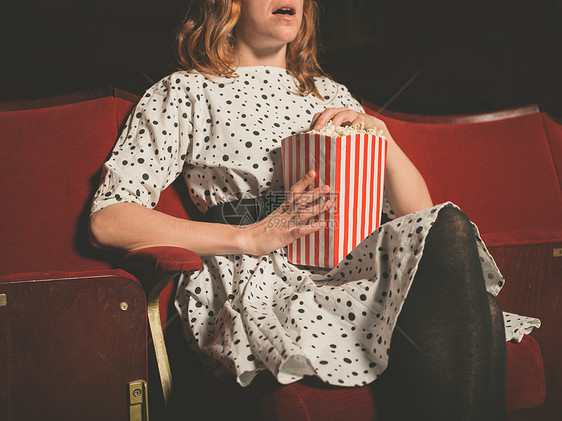 个轻的女人坐电影院的前排,边吃爆米花边看部令人兴奋的电影图片