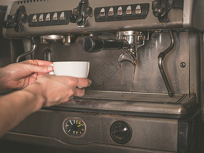 个轻女人的手把个杯子放专业咖啡机的分配器下图片