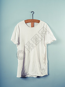 件白色的t恤挂个木制衣架上,靠蓝色的墙上图片