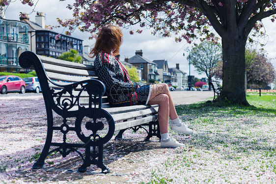个轻的女人坐公园的长凳上,地上开着樱花图片