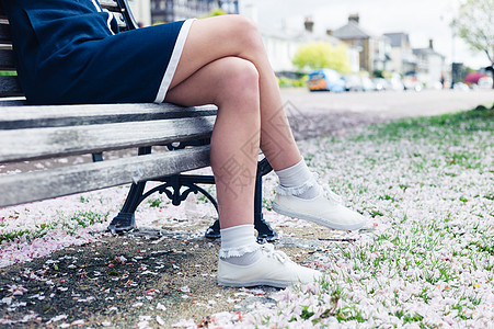 个轻女人的腿脚公园的长凳上放松,地上开着樱花背景图片