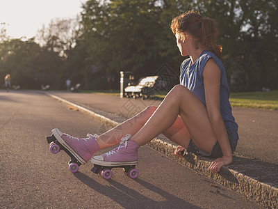 个轻的女人日落时坐公园里的地上,她穿着溜冰鞋图片