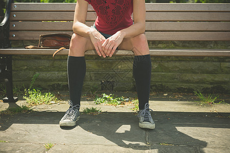 个穿着膝盖高袜子的轻女人坐公园的长凳上图片