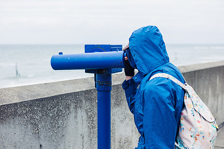 个穿着蓝色夹克引擎盖的人正海岸上用望远镜图片