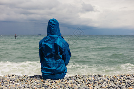 个穿着蓝色夹克的人刮风的日子坐海滩上图片