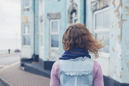 个刮风的日子里,个轻的女人站海边所蓝色房子外的街上图片