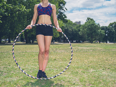 个健康的轻女人站阳光明媚的夏天公园里的草地上,着个呼啦圈图片