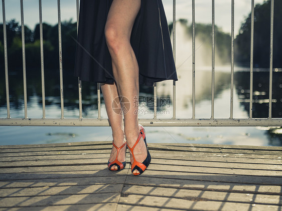 位优雅的女人站公园湖边的码头上,用老式的过滤镜头拍摄了她的腿脚图片