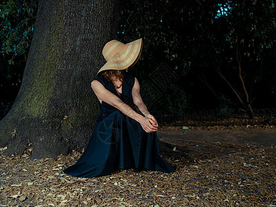 个优雅的女人穿着连衣裙帽子公园的棵树下放松图片