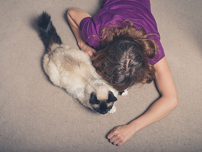 位轻女子躺家里的地毯上,抚摸着只猫图片