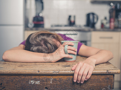 个疲惫的轻女人正喝杯茶,把头靠桌子上图片