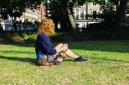 个阳光明媚的夏天,个轻的女人坐城市公园里的草地上图片