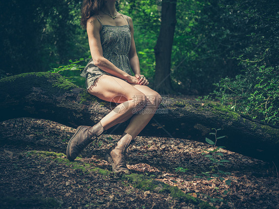 个光着腿的轻女人坐森林里的根木头上图片