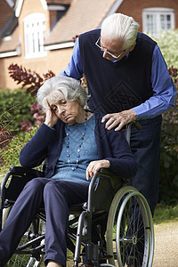坐轮椅的沮丧的老妇女被丈夫推着图片