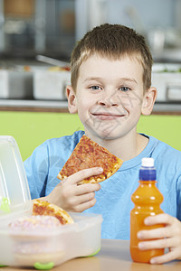 男学生坐学校自助餐厅的桌子上吃健康的包装午餐图片
