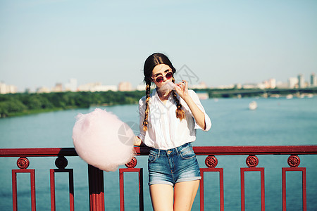 生活方式轻快乐的时髦女人吃着甜棉花糖,桥上俯瞰城市的美景图片