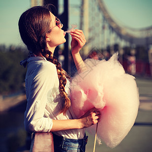 生活方式轻快乐的时髦女人吃着甜棉花糖,桥上俯瞰城市的美景图片