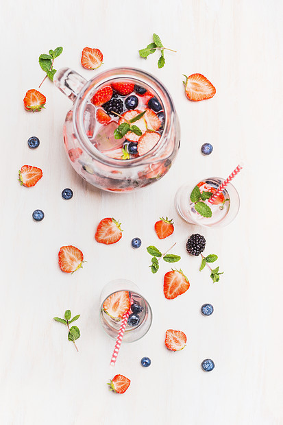 夏天喝浆果冰块水壶水罐与浆果柠檬水,眼镜,吸管配料白色的木制背景,顶部视图健康的维生素饮料图片