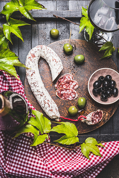 静态生活与典型的意大利反意大利萨拉米,各种橄榄,葡萄叶红酒黑暗的木制厨房桌子上,顶部视图意大利食物图片