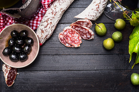 切片意大利腊肠与绿色黑色橄榄,安帕斯蒂红酒黑色木制背景,顶部视图,地点为文本意大利食物背景图片