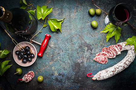意大利静物与意大利腊肠,红酒,橄榄葡萄叶黑暗的乡村背景,顶部的视野,文字的地方意大利食物背景图片