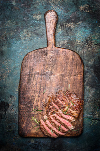切片烤牛肉烧烤牛排木制切割板上的乡村背景,顶部视图图片